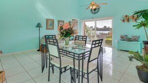 A dining area with a glass table and chairs, a ceiling fan, and a view of the outdoors.