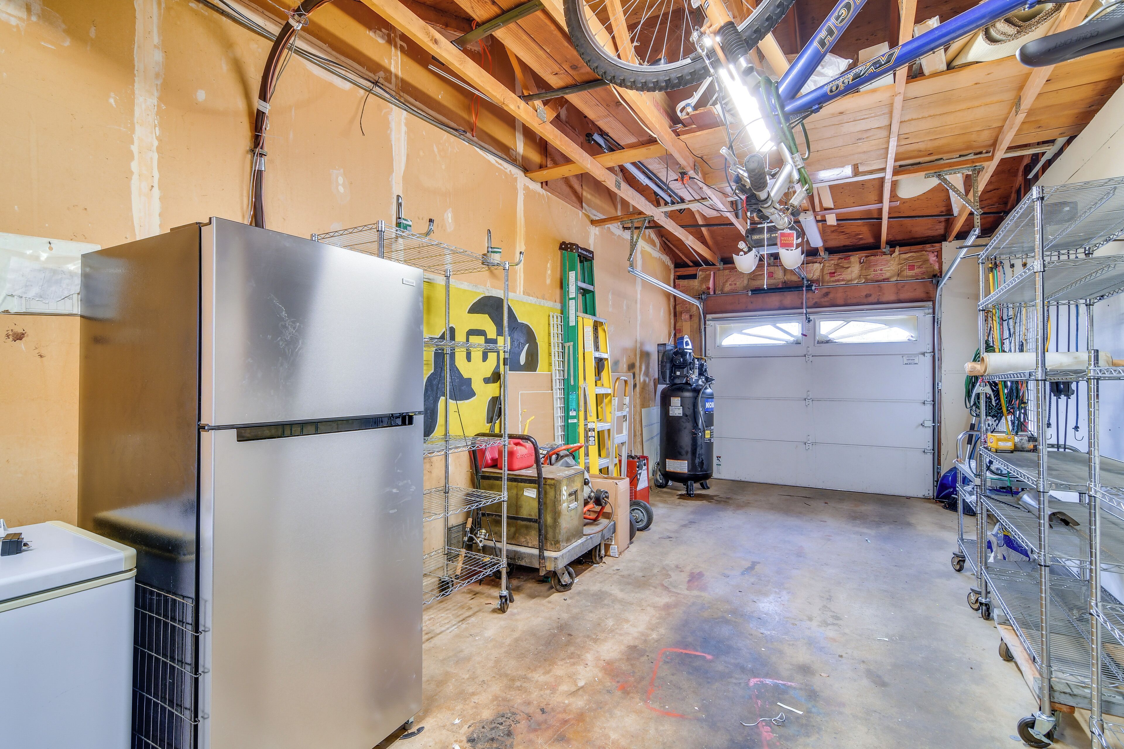 A garage with a large refrigerator, shelving units, and a bicycle mounted on the ceiling.