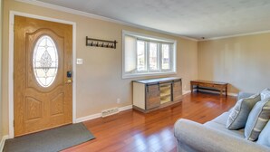 Un salón con piso de madera, una puerta de madera con ventanal y un banco, además de un sofá con cojines.