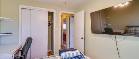 A bedroom with a bed, a desk, a chair, a ceiling fan, and a mirror.