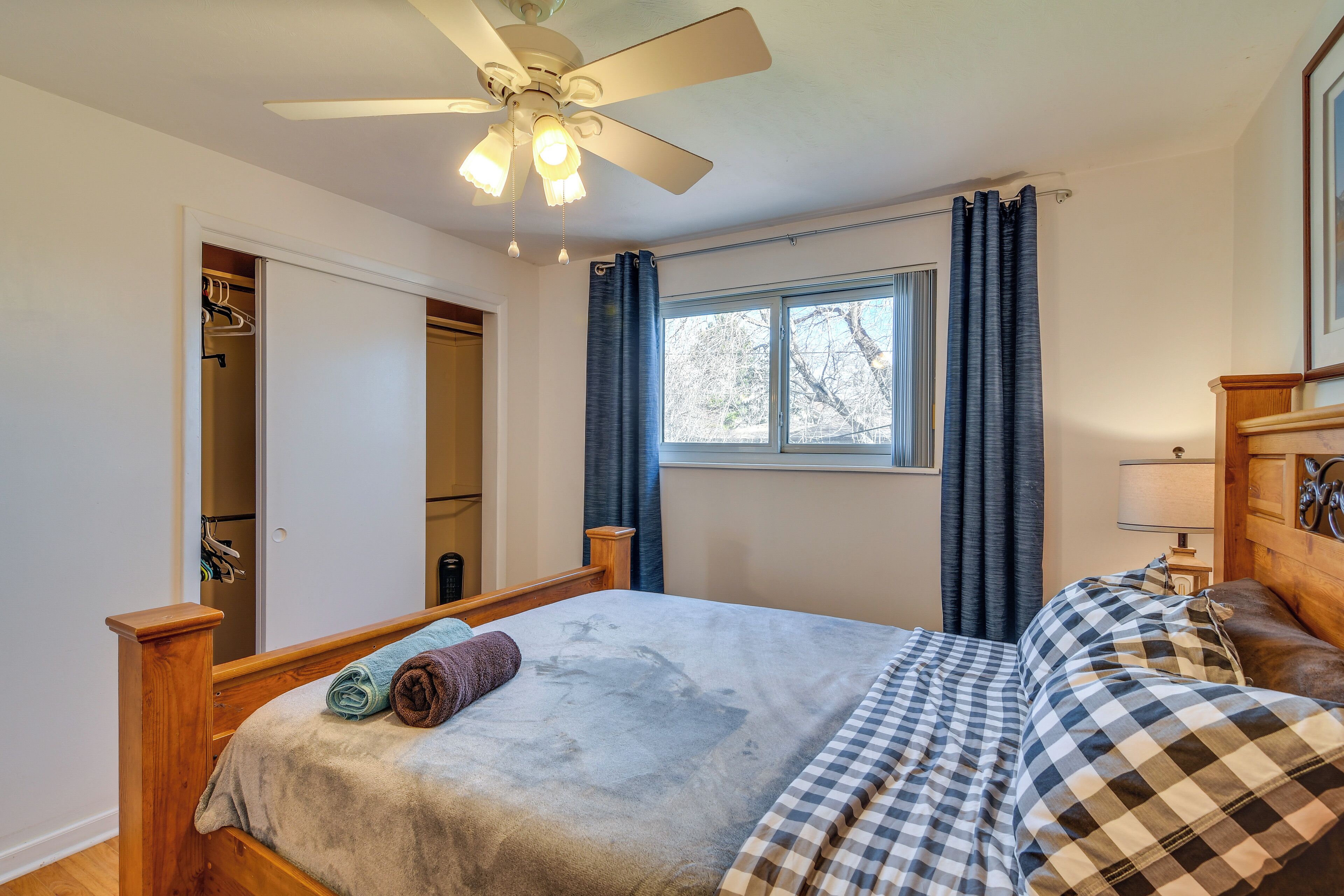 A bedroom with a bed, a ceiling fan, a window with curtains, and a wardrobe.