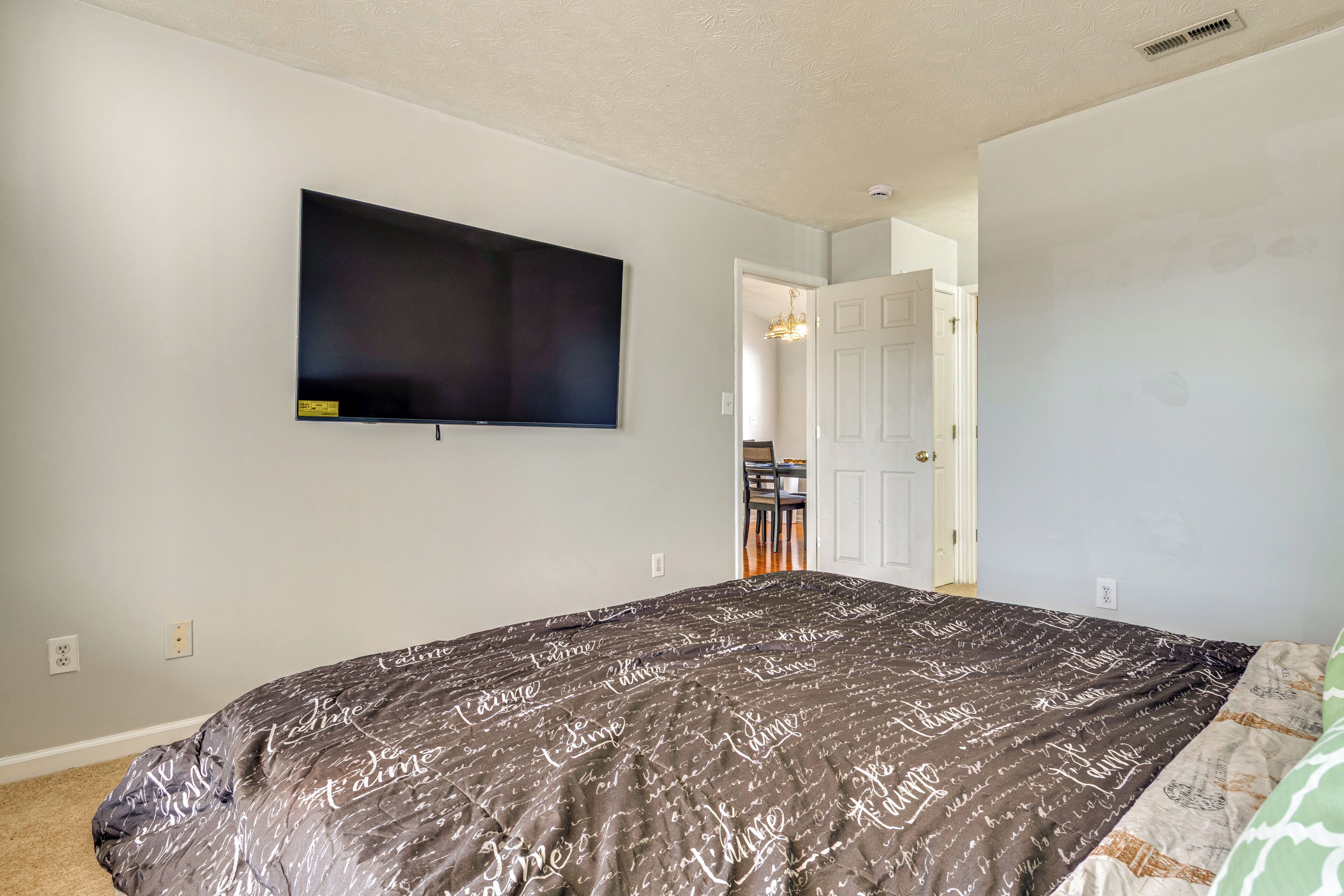 A bedroom with a large bed, a flat-screen TV mounted on the wall, and a door leading to another room.