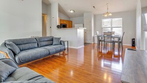 Ein modernes Wohnzimmer mit einem grauen Sofa, Holzboden und einem Essbereich mit Tisch und Stühlen.