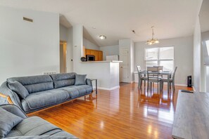 A modern living room with a grey sofa, wooden flooring, and a dining area with a table and chairs. - Quiet + Convenient! 2-story Townhouse in NW Indy (Indianapolis)