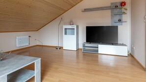 A spacious living room with a sloped ceiling, a white entertainment unit, a flat-screen TV, and a radiator. - Helfrichs Ferienwohnung by Interhome (Pirmasens)