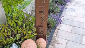 A metal sign with text, surrounded by greenery and a paved path. - Helfrichs Ferienwohnung by Interhome (Pirmasens)