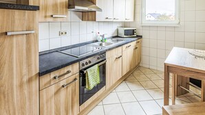 A modern kitchen with wooden cabinets, a black countertop, a stainless steel range hood, a microwave, and a window with a view of buildings. - Helfrichs Ferienwohnung by Interhome (Pirmasens)