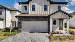 A two-story house with a garage, stone facade, and a well-maintained lawn. - Reunion Resort: Brand-new Home Near Disney! (Kissimmee)