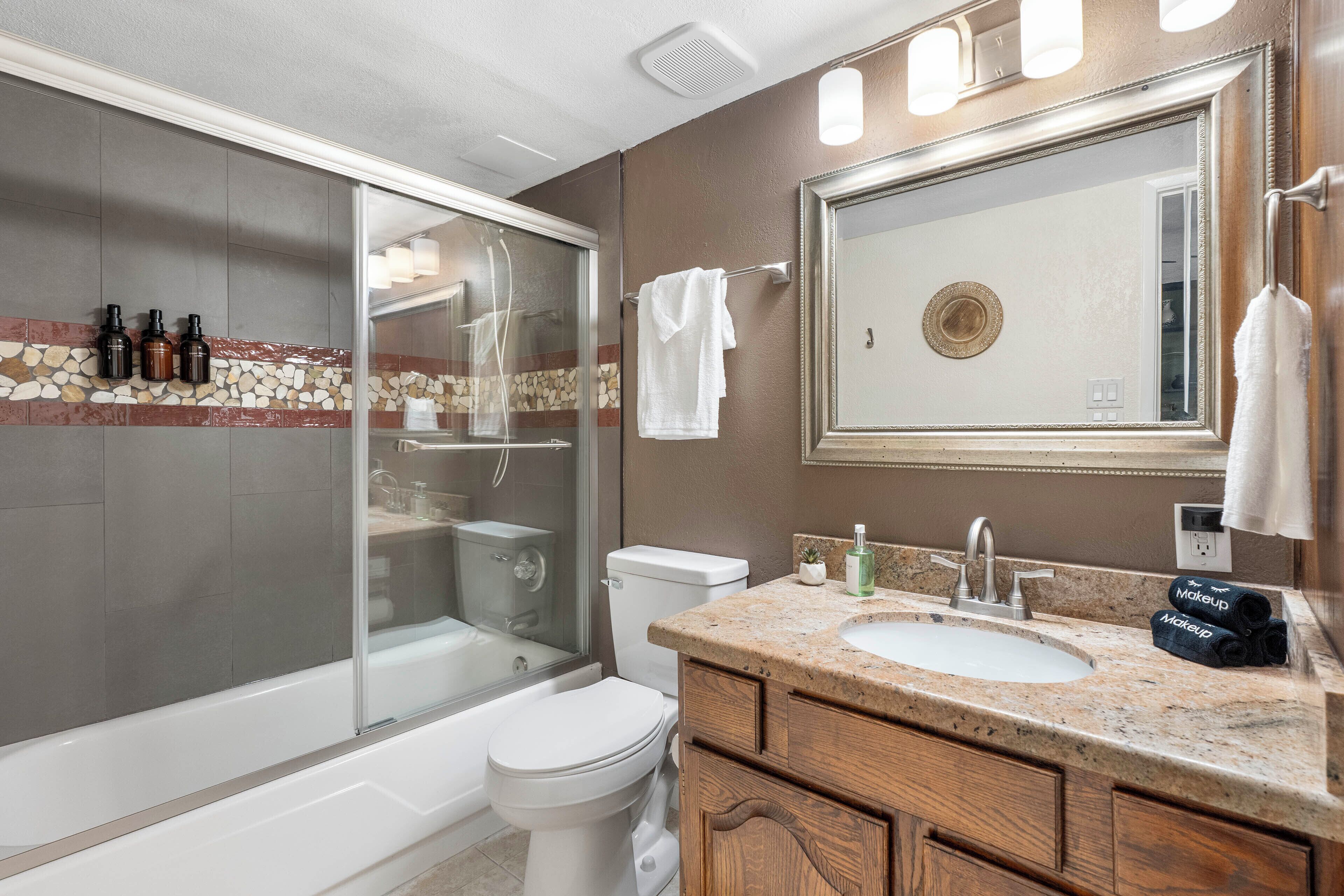 A bathroom with a glass shower enclosure, a white toilet, a sink with a vanity, and a large mirror.