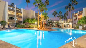A swimming pool with palm trees and lounge chairs, surrounded by a multi-story building with balconies. - Walk to Old Town & Fashion Square, Condo w/ Patio! (Scottsdale)