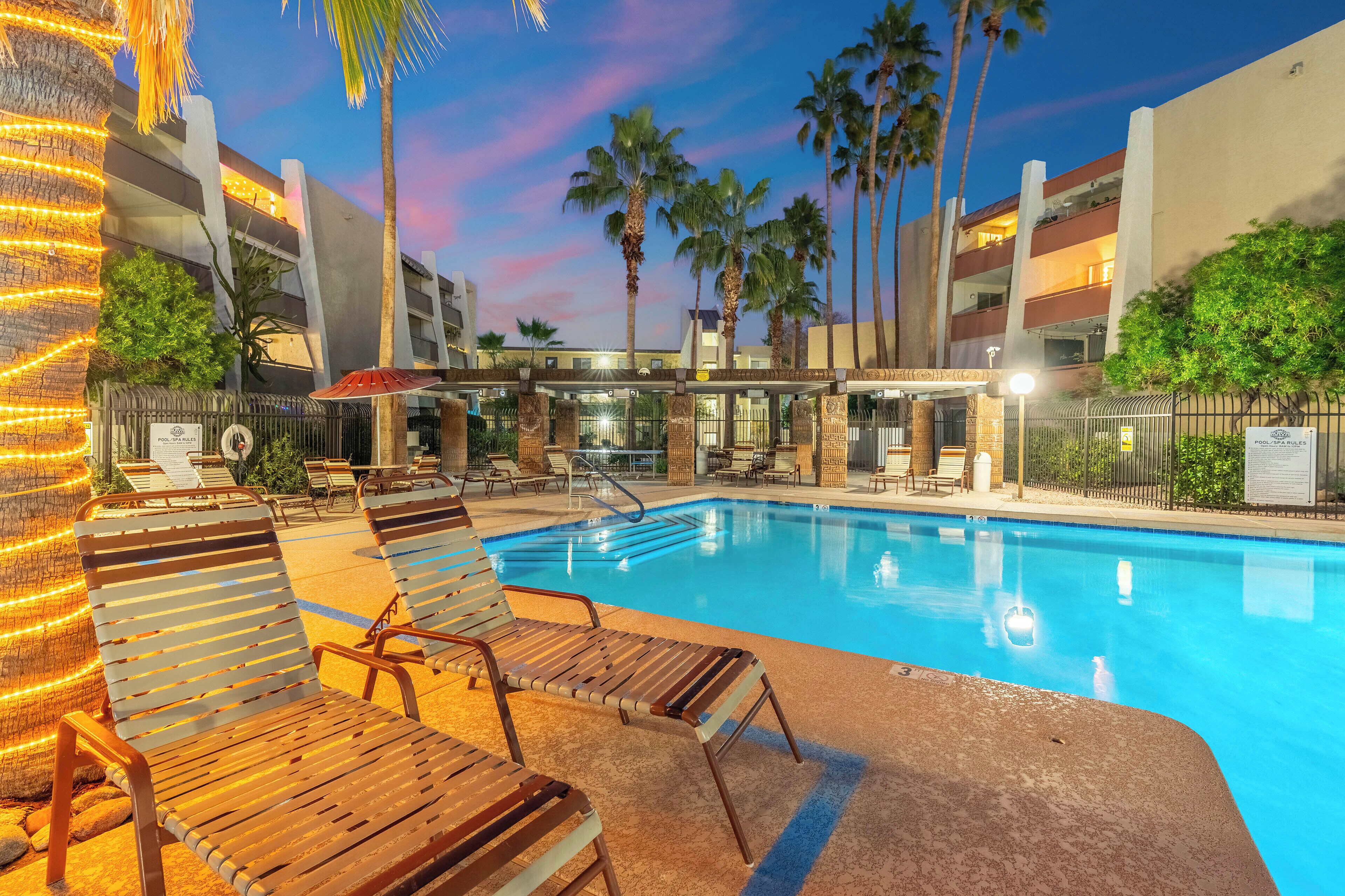 Un espace piscine avec des chaises longues, des palmiers et un bâtiment doté de balcons.