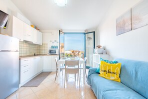 A bright kitchen with white cabinets, a dining table with chairs, and a blue sofa with a yellow pillow. - Affittimoderni Valledoria - Malù House (Valledoria)