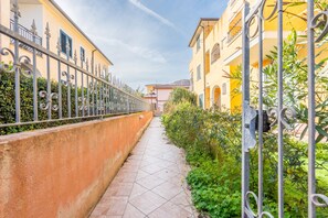 A narrow alleyway with a tiled floor, bordered by a low wall and metal fencing on one side, and a building with balconies on the other. - Affittimoderni Valledoria - Malù House (Valledoria)