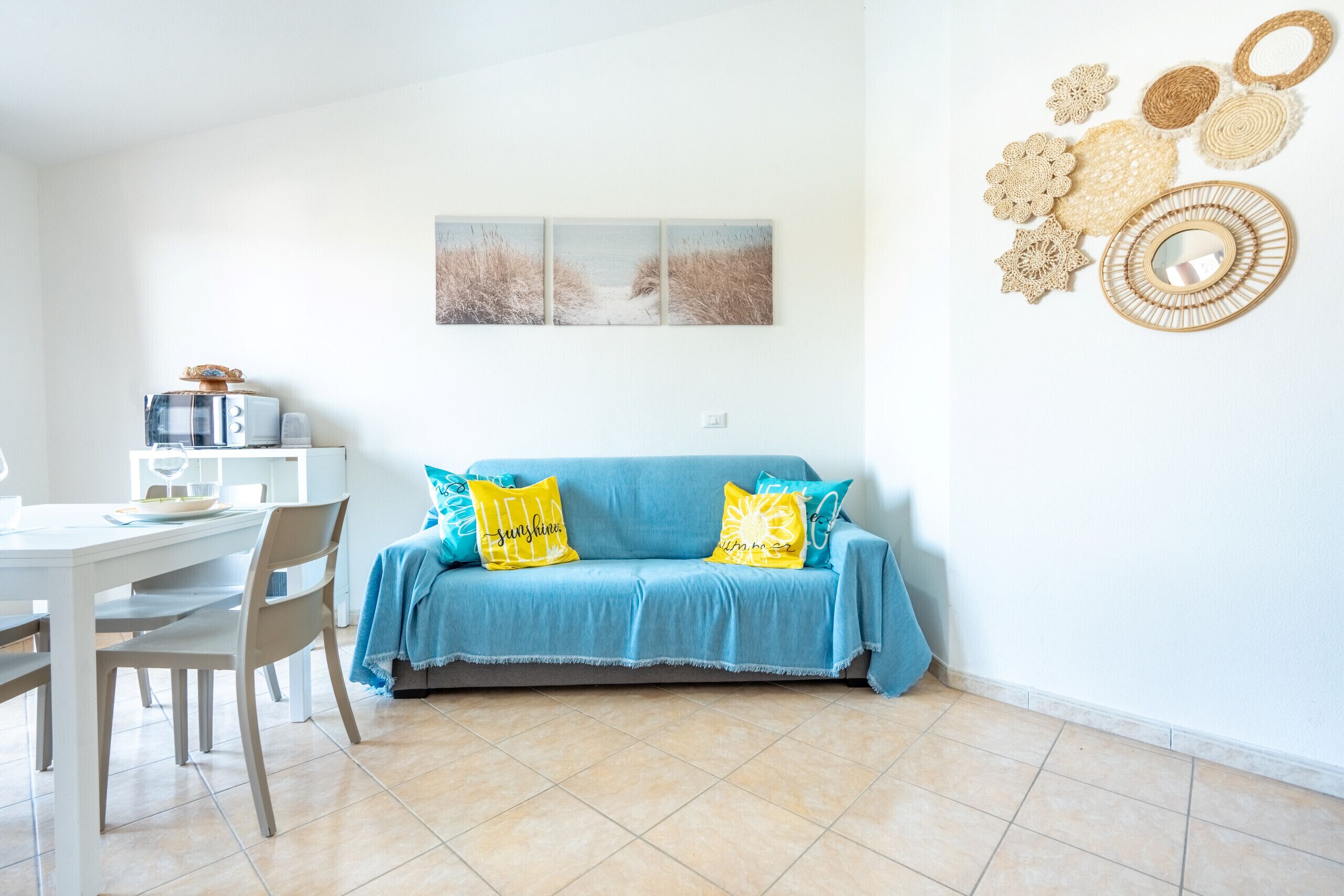 A living room with a blue sofa, two yellow cushions, a white coffee table, and a dining area with a white table and chairs.