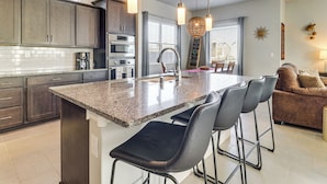 Una cocina moderna con encimeras de granito, electrodomésticos de acero inoxidable y una isla central con taburetes de bar.