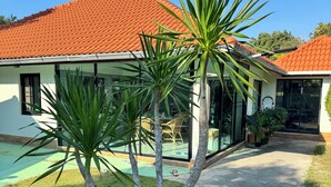 Een huis met een pannendak, een zwembad en een verzorgd gazon met palmbomen.