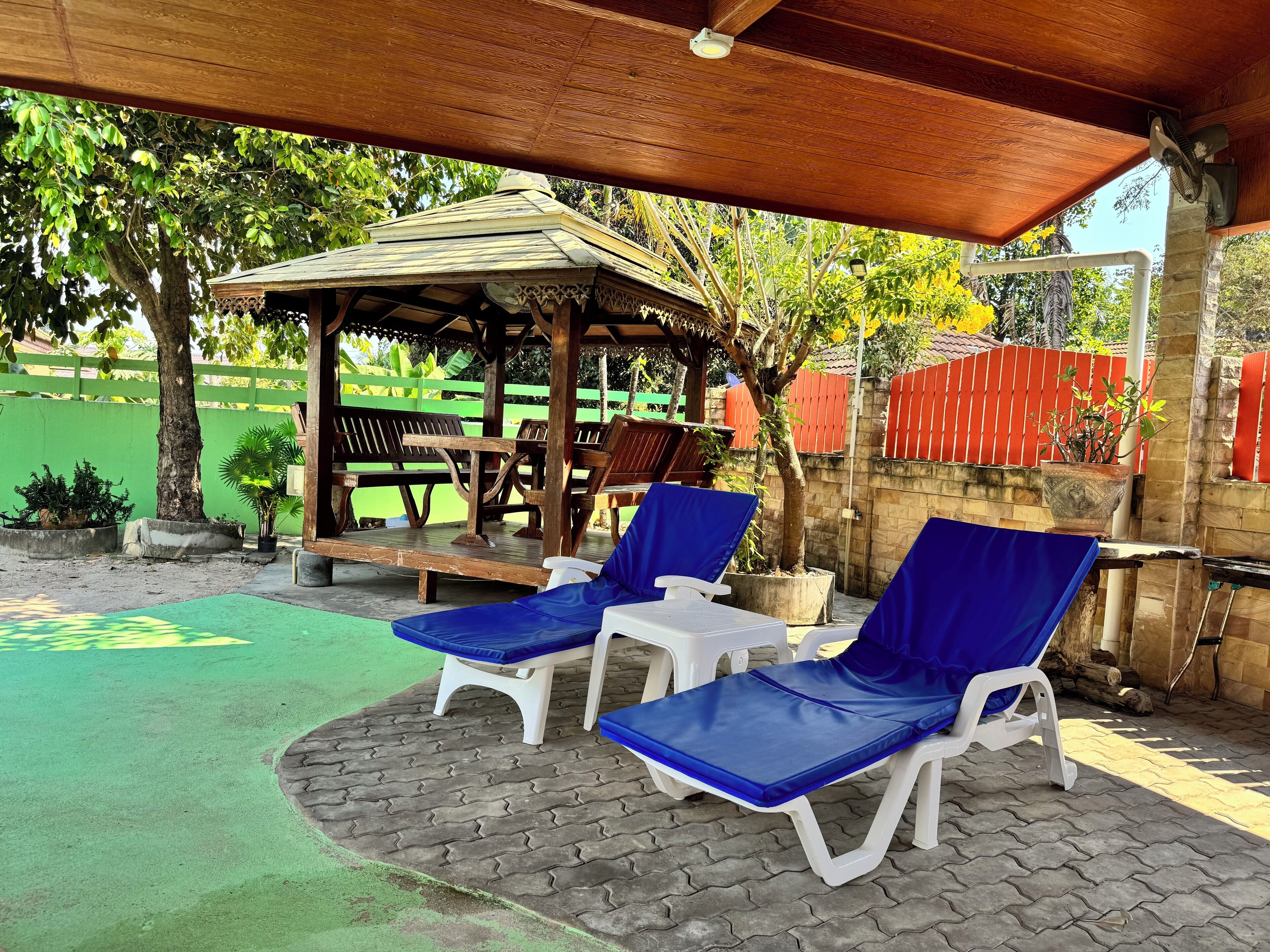 A covered outdoor seating area with two blue cushioned chairs and a small table.