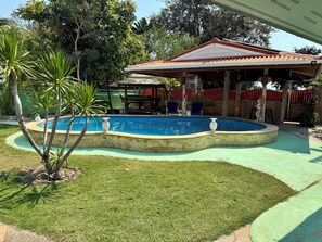 Una piscina amb terrassa enrajolada, envoltada d'herba i arbres.
