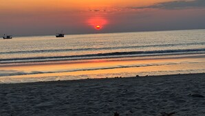Een strand met een ondergaande zon, rustige zee en boten.