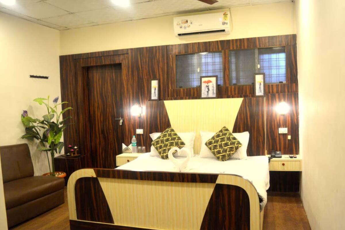A hotel room with a bed, a nightstand, a plant, and a sofa.