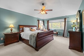 A bedroom with a large bed, a ceiling fan, a nightstand with a lamp, a dresser, and a window with curtains. - New Listing! Pinery Lakeshore Retreat | Near Park (Parker)