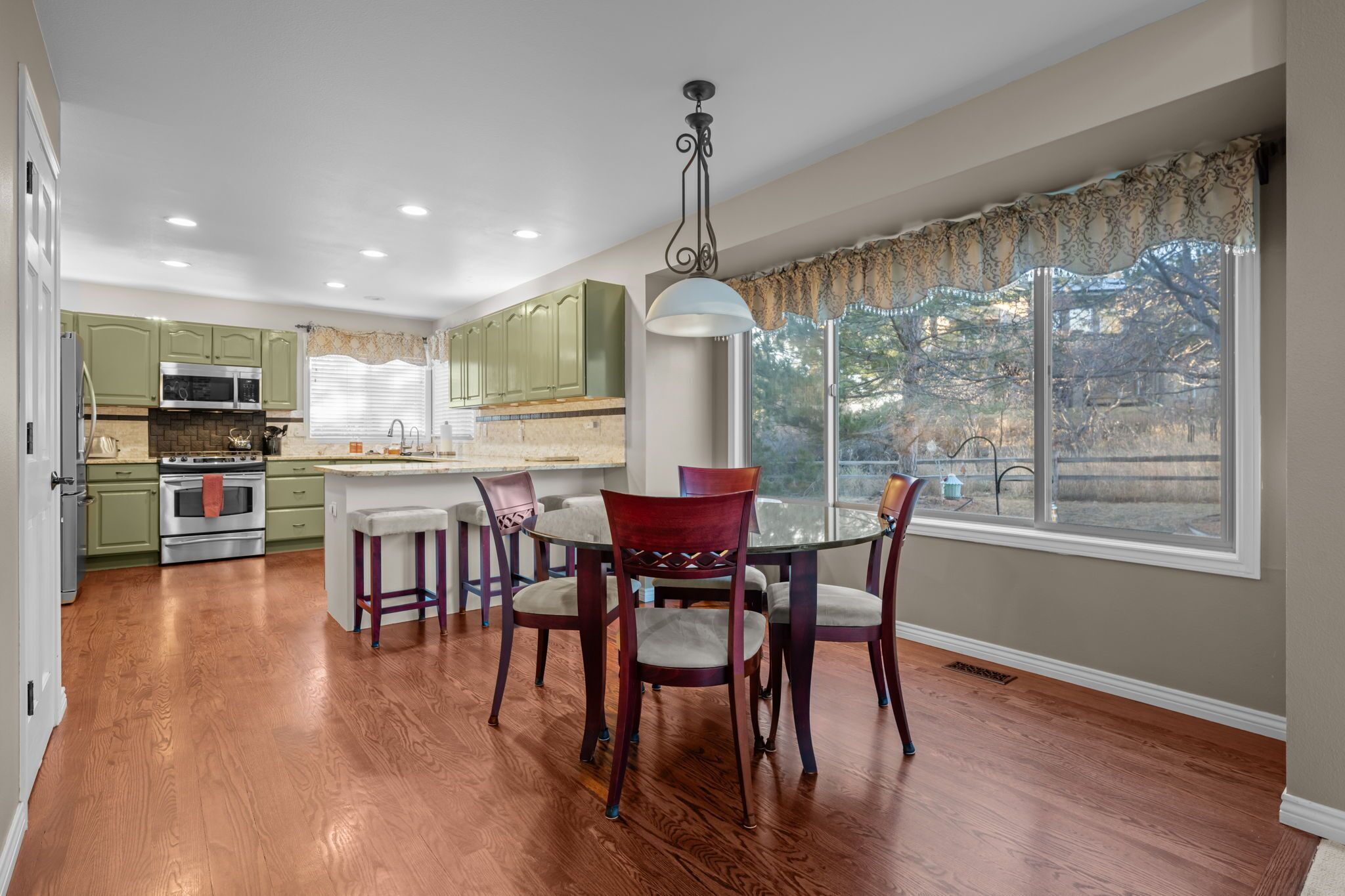 A modern kitchen with green cabinets, a central island, and a dining area with a round table and red chairs.