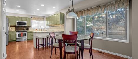A modern kitchen with green cabinets, a central island, and a dining area with a round table and red chairs.