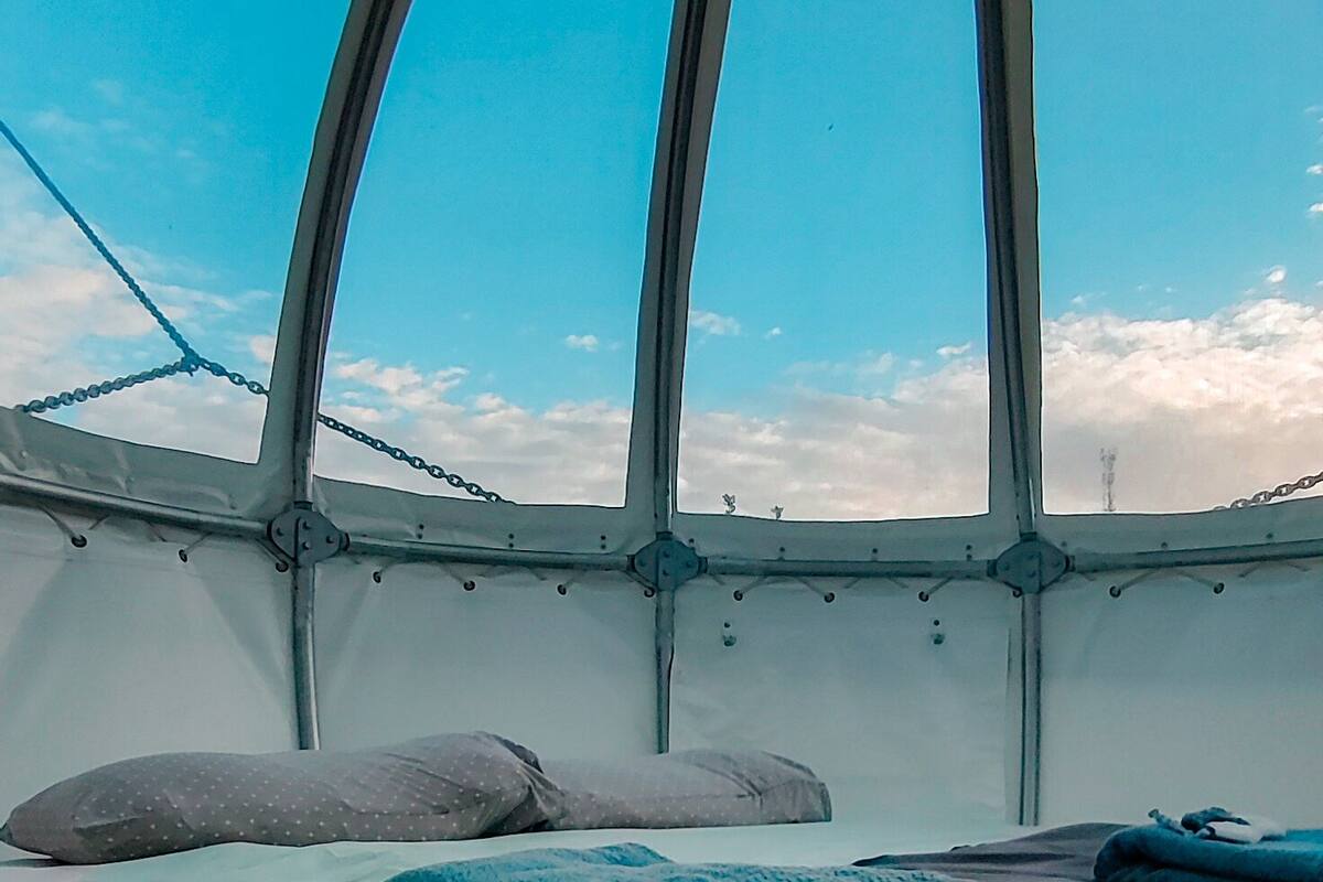 Una habitación con cama, almohadas y vistas a través de un ventanal.