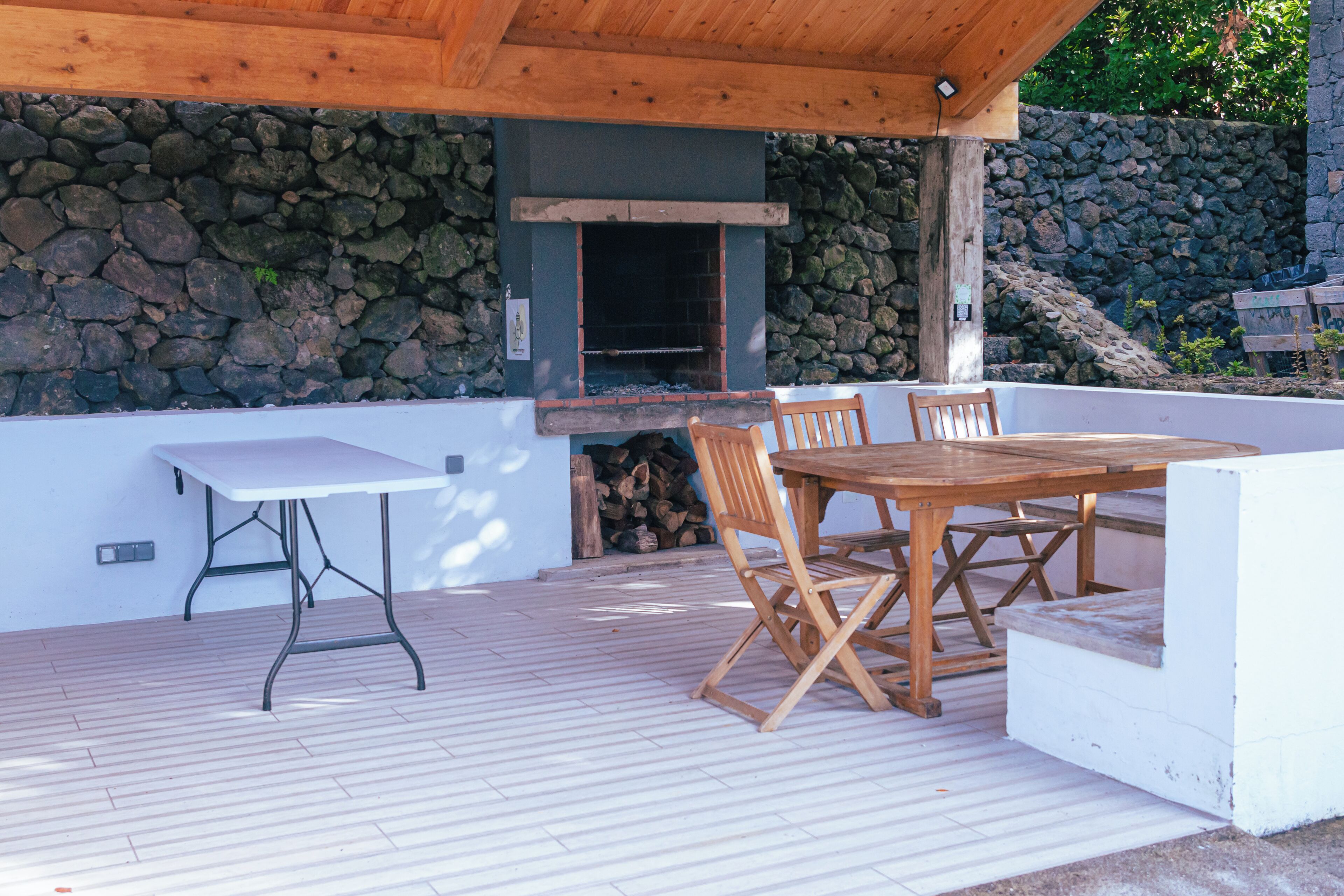 An outdoor patio with a stone wall, a wooden table and chairs, and a grill area.