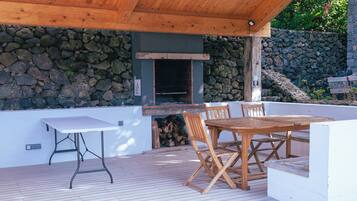 An outdoor patio with a stone wall, a wooden table and chairs, and a grill area.