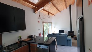 A modern kitchen with black cabinets, a glass island, and a built-in dishwasher. There is a blue sofa and a TV in the living area. - Quinta do Abacate (Angra do Heroismo)