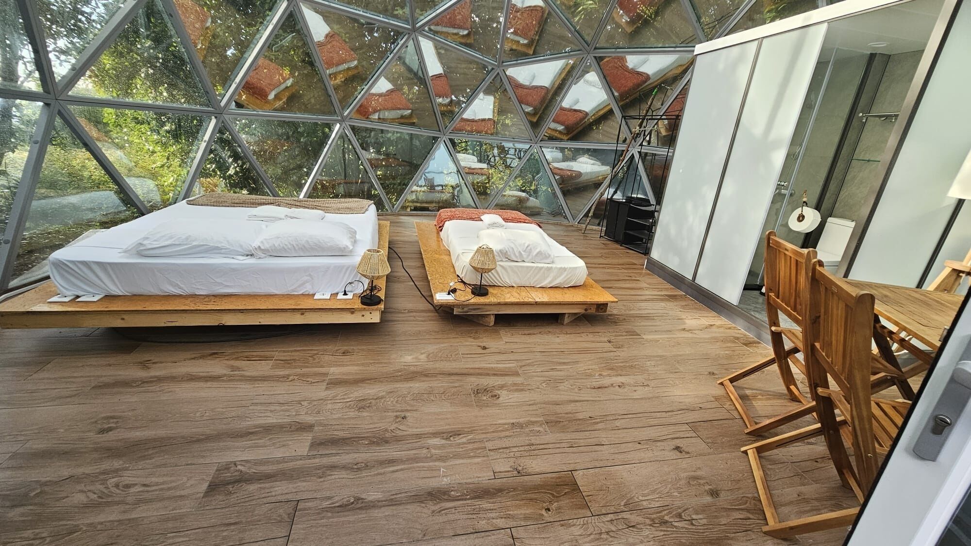 Ein moderner Raum mit Glaswänden, zwei Holzbetten und einem Holzstuhl.