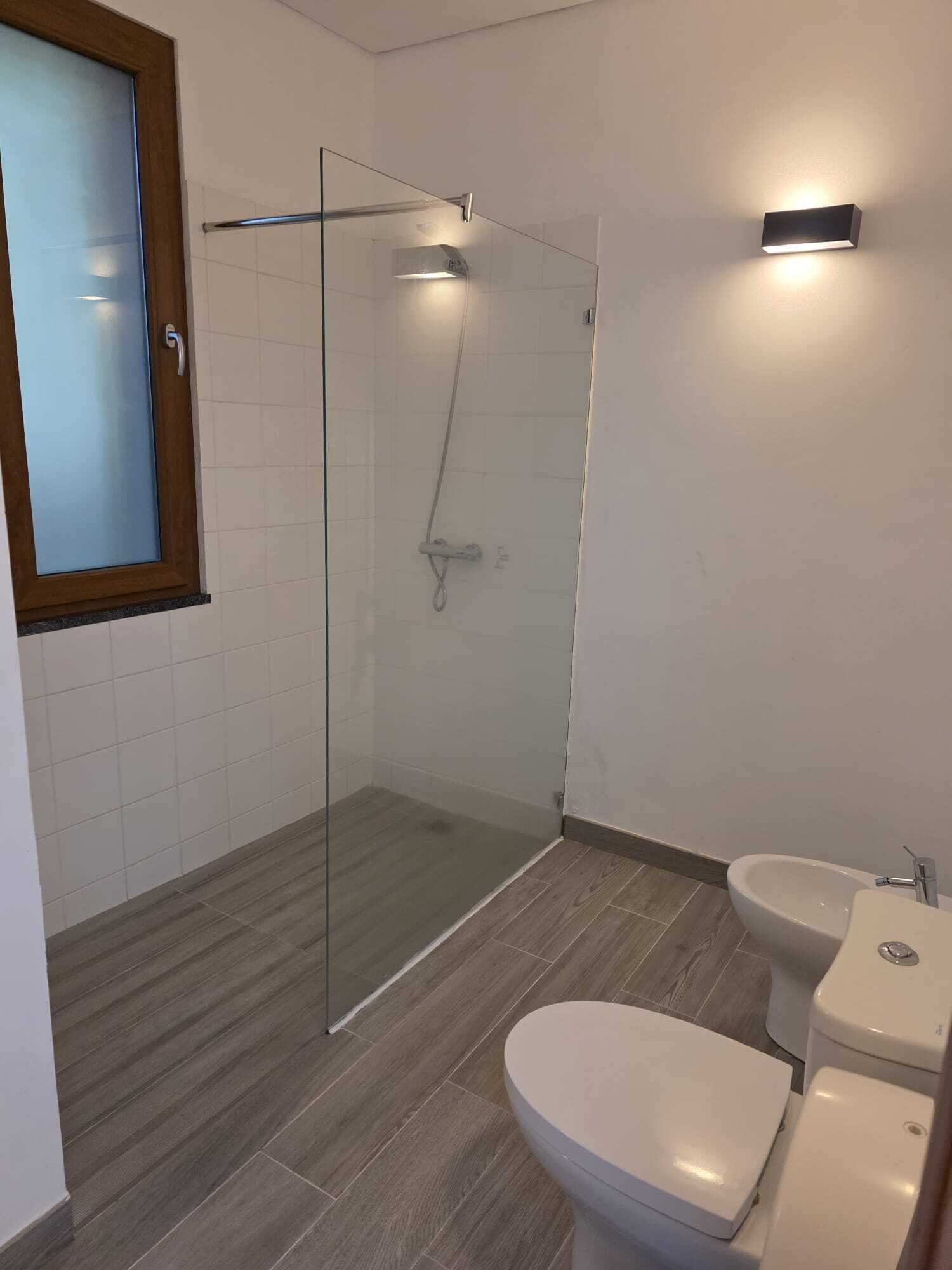 A modern bathroom with a glass-enclosed shower, a toilet, and a bidet.