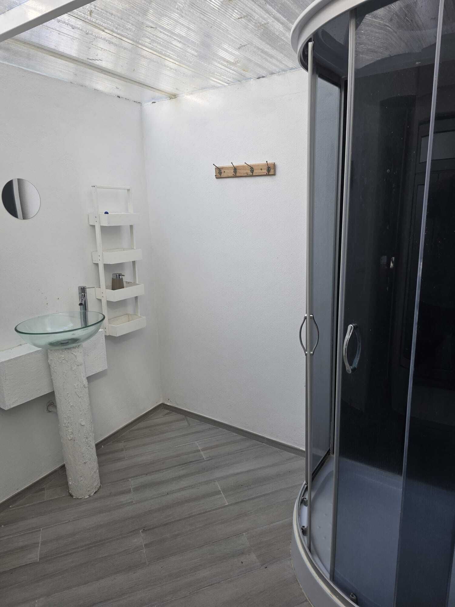 A bathroom with a glass sink, a white vanity, a wooden shelf, and a glass shower enclosure.