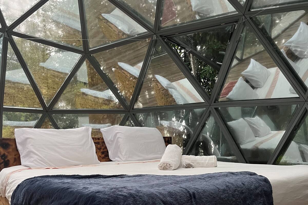 Una cama con almohadas blancas y una manta azul oscuro en una habitación con techo de vidrio geométrico.