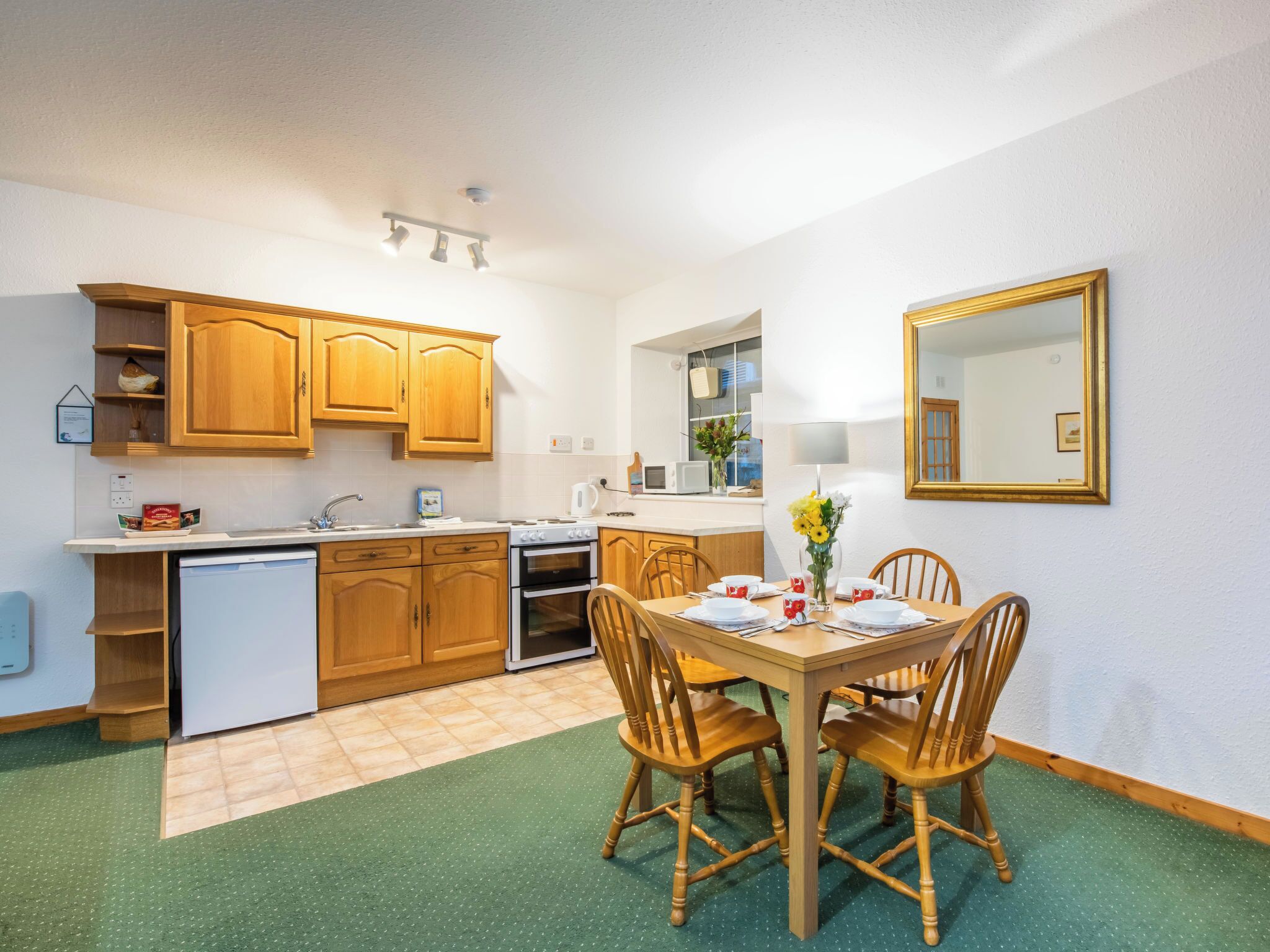 A compact kitchen with wooden cabinets, a built-in dishwasher, and a dining area with a table set for four.
