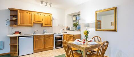 A compact kitchen with wooden cabinets, a built-in dishwasher, and a dining area with a table set for four.