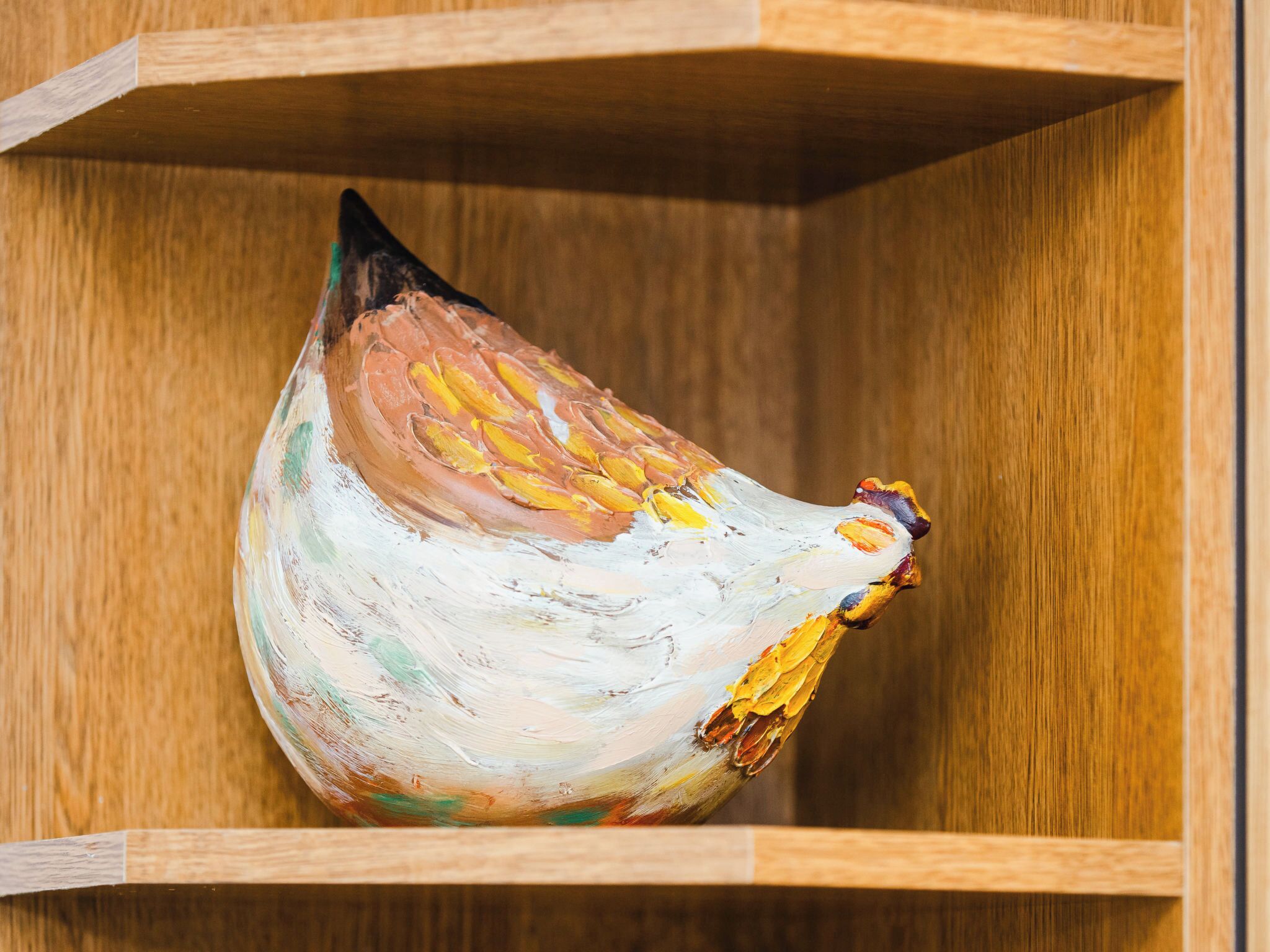 A wooden shelf with a painted ceramic rooster.