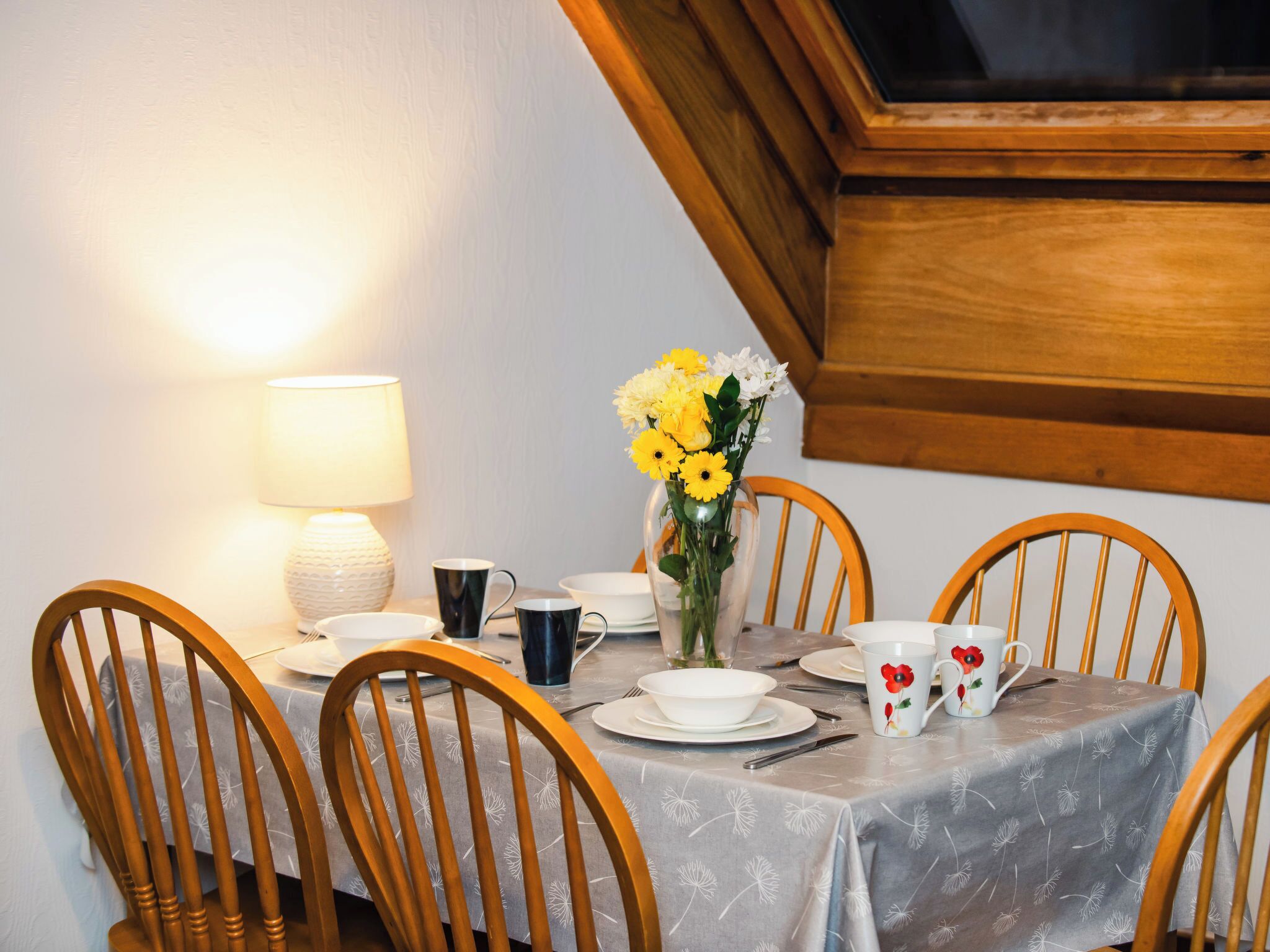 Una mesa de comedor dispuesta con sillas, un jarrón de flores y una lámpara.