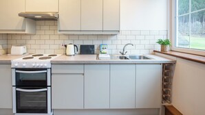 Une cuisine moderne avec des meubles blancs, un four encastré, une cuisinière, une bouilloire et un évier.