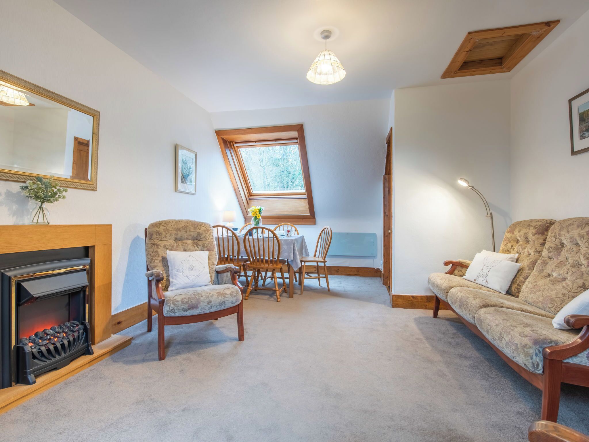 Een gezellige woonkamer met een open haard, een bank, een eettafel met stoelen en een dakraam.