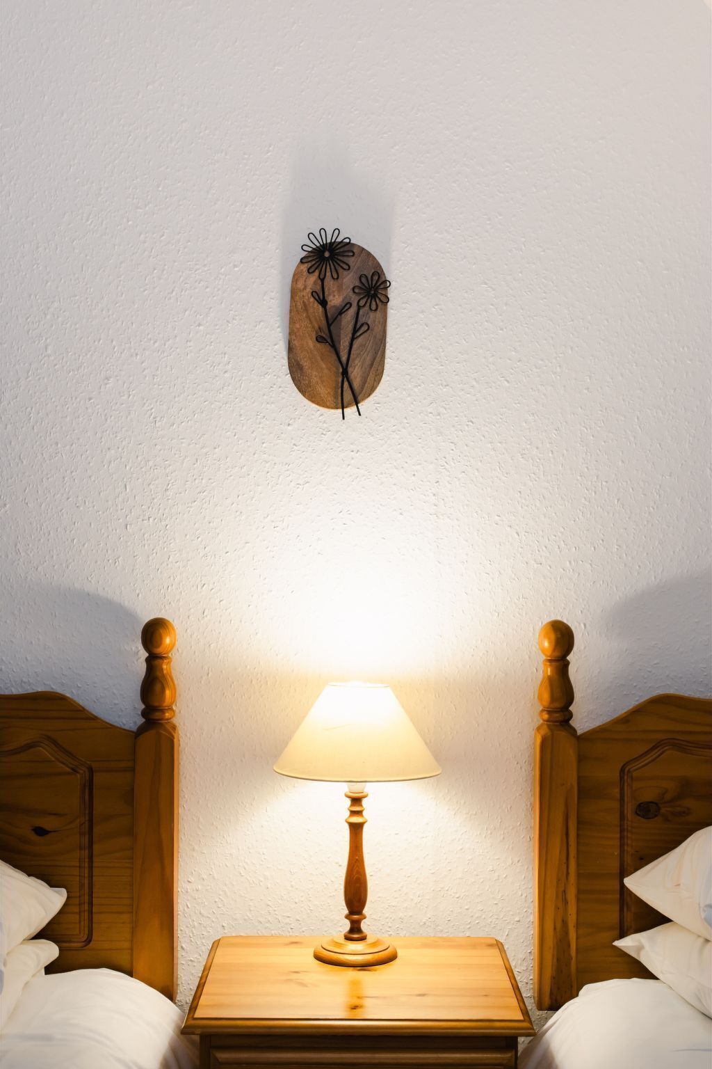 Een slaapkamer met een houten nachtkastje, een bedlamp en een houten decoratie aan de muur.