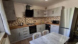 A compact kitchen with a tiled backsplash, a gas stove, a microwave, a washing machine, and a refrigerator.