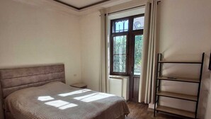 A bedroom with a bed, a window with curtains, a radiator, and a shelf unit.
