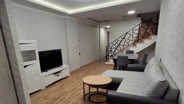 A modern living room with a sectional sofa, a round coffee table, a flat-screen TV, and a staircase with a geometric railing.