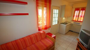 A compact living space with a sofa, a kitchenette, and a television. - Cozy Villa Close to the Beach (Lignano Sabbiadoro)