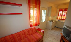 A compact living space with a sofa, a kitchenette, and a television. - Cozy Villa Close to the Beach (Lignano Sabbiadoro)