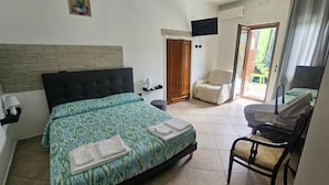 Una habitación de hotel con cama, una silla, escritorio, televisor y puerta que da a un balcón.