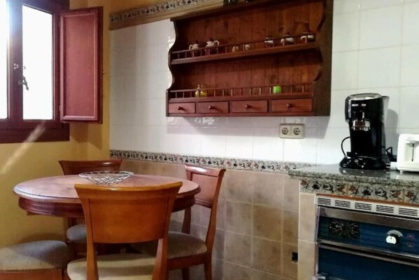 A kitchen with a wooden table and chairs, a coffee maker, and a tiled backsplash.