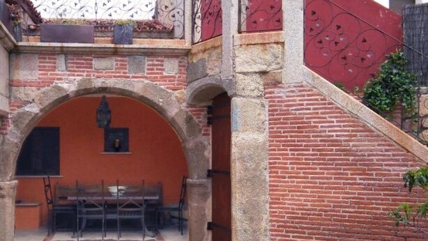 An outdoor patio area with a brick wall, a wooden table, and chairs. - Tictágora House: House 1 (Plasenzuela)